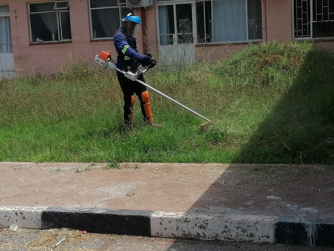 Worker cutting overgrown grass around a building
